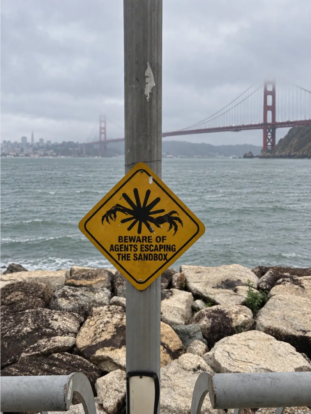 AI Governance Where to Start 4 Yellow sign reading ‘Beware of agents escaping the sandbox’, with the Golden Gate Bridge in the background.